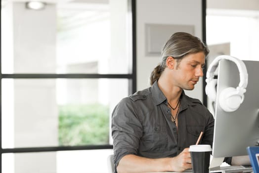 Young man in casual sitting at desk and working on computer