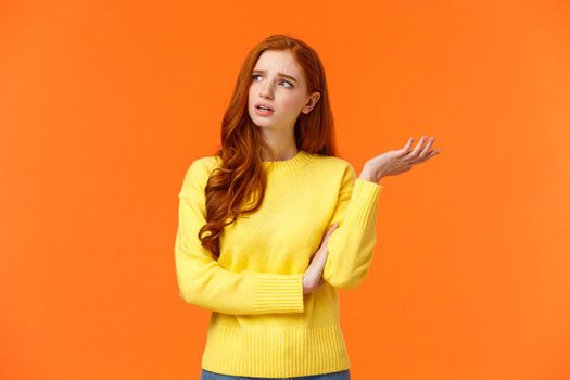 Troubled and unsure, indecisive cute redhead girl trying solve problem, searching resolve, looking perplexed upper left corner pondering, raise hand uncertain, confused, shrugging, orange background.