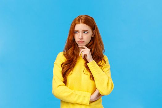 Sad timid and lonely redhead woman too feeling let down and depressed, sulking looking upset and envy left, frowning touching lip pensive, having bad feeling, standing anxious over blue background.
