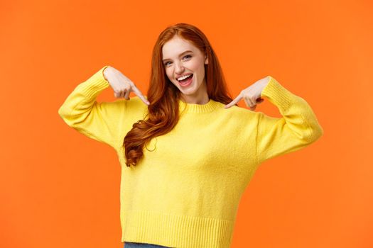 Confident and energized, good-looking redhead woman pointing at herself, introducing personal achievement, bragging or being proud, volunteer, feeling upbeat, smiling, orange background.