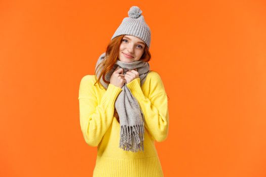 Tender gorgeous redhead female feeling comfortable and warm, got valentines gift cute hat and lovely scarf, tilt head smiling camera joyful, standing enthusiastic and happy orange background.