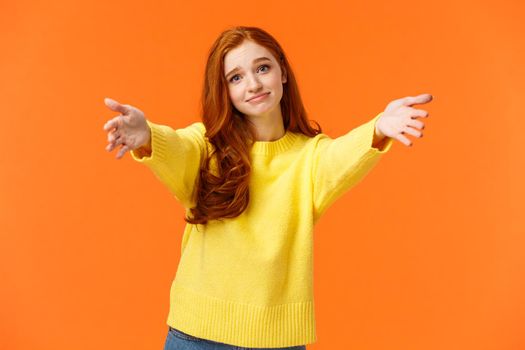 Girl asking come here to give cheer-up hug. Cute and touched tender redhead woman in yellow sweater, extend arms,stretch hands forward for cuddle, embrace friend, smiling lovely, orange background.