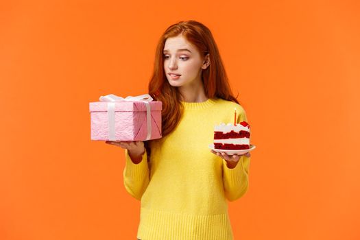 Celebration, presents and holidays concept. Cute redhead girl looking with temptation, desire at gift box, holding wrapped present, piece of delicious b-day cake, birthday girl want unwrap surprise.