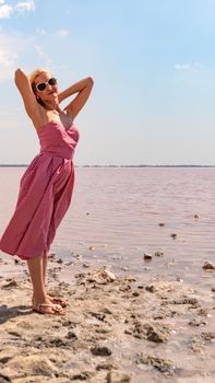 Cheerful lady in a red dress young smiling at the camera against the background of a red lake with blue clouds in hot sunny weather