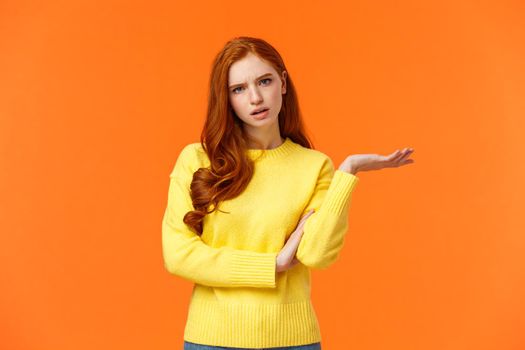 Skeptical and troubled, uncertain young redhead woman cant understand how resolve proble, shrugging raise hands sideways, frowning confused or unsure, standing frustrated orange background.