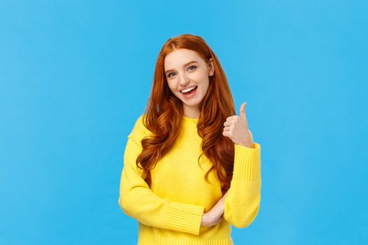 Wonderful idea. Supportive cute redhead girlfriend encourage you try, approve good choice, smiling pleased, nod approval and showing thumb-up like gesture, stand blue background.