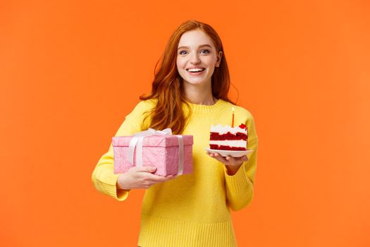 Holidays, celebration and people concept. Cheerful gorgeous redhead girlfriend receive cute gift, holding present in wrapped box and piece cake with candle, smiling celebrate birthday, b-day party.