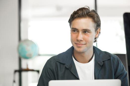 Young man in casual sitting at desk and working on computer
