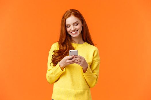 Communication, people and chat concept. Carefree modern hipster girl edit photos with filters on smartphone application, use app for chatting, smiling as looking mobile display, orange background.