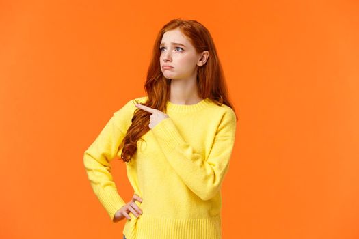 Jealous or envy sad sulking redhead girl in yellow sweater looking at desired thing, shoppaholic cant buy, dont have money, pointing and staring upper left corner with moody unhappy face.