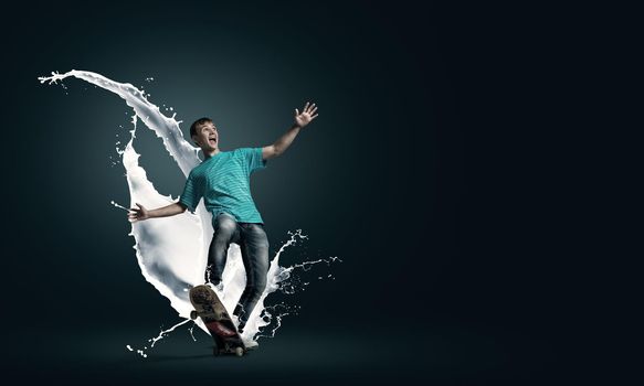 Young guy riding skateboard and paint splashes from under wheels