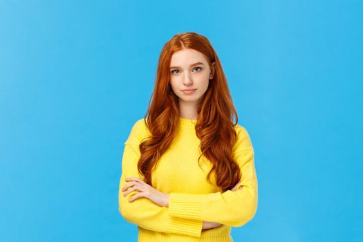 Professionalism, e-commerce and business concept. Serious-looking determined smart gorgeous redhead woman in yellow sweater, cross arms chest confident, looking camera, blue background.