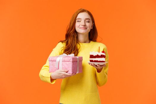 Celebration, people and b-day concept. Dreamy upbeat and tender redhead woman celebrating birthday, holding piece cake with candle and close eyes happy, hold cute pink wrapped box gift.