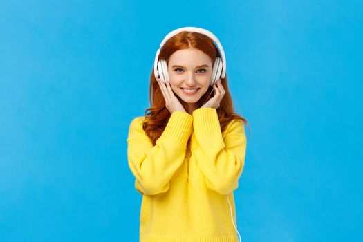 Waist-up shot sassy good-looking redhead, ginger girl with blue eyes and freckles in soft yellow sweater, listen music headphones, press earphones to ears, smiling hear new song favorite singer.