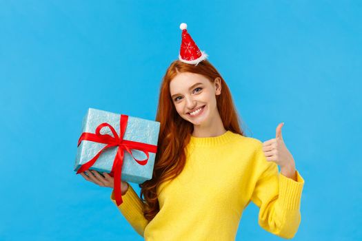 Girl can wrap your gift easily. Pleased and assertive pretty redhead female shop assistant help out customer, showing thumb-up, all done or good gesture, smiling holding box of present.
