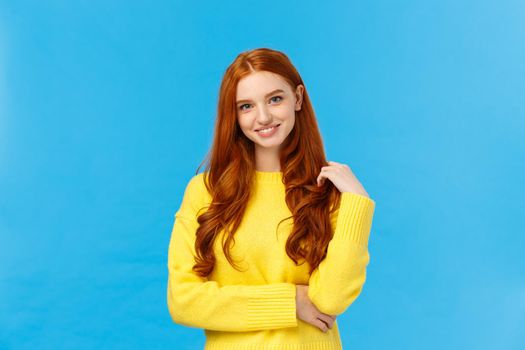 Waist-up shot attractive flirty redhead modern girl millennial in yellow sweater, playing with hair and smiling lovely with entertained, curious expression, looking camera having conversation.