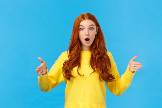 Woman impressed with enourmous size of present. Wondered and amused good-looking redhead girl in yellow winter sweater, shaping big object, showing length or distance with stretched hands.