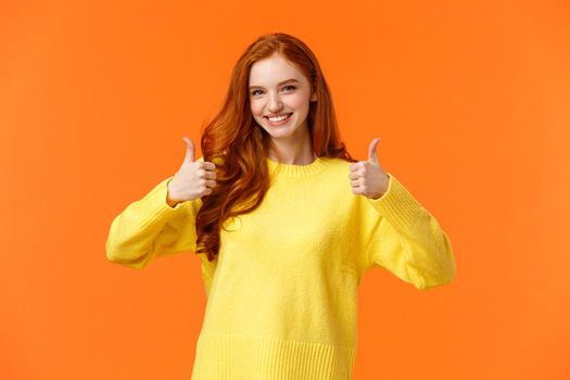 Confident and caring good-looking redhead sister rooting for sibling, saying yes, approving choice, recommend product, show thumbs-up and nod acceptance, smiling positive reply, orange wall.