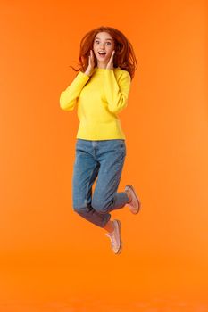 Emotions, holidays and people concept. Full-length vertical portrait cute and silly jumping redhead female student look amused and excited, hear amazing news, gasping stare camera impressed.