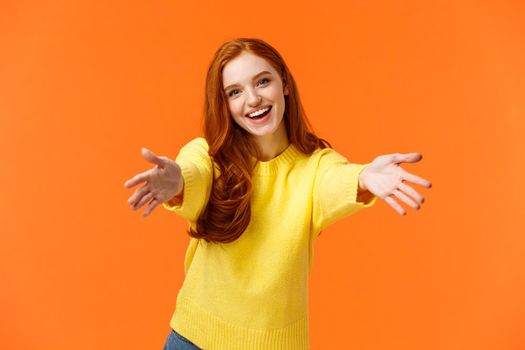 Holidays, family and relationship concept. Tender, gorgeous redhead woman, lovely girlfriend extend arms reaching for someone, want hug, embrace friend, smiling lovely and kind, orange background.
