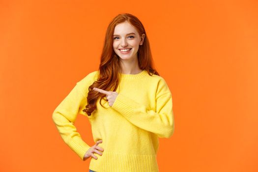 Shopping, consumer and holidays concept. Cheerful attractive redhead woman in yellow sweater invite check-out shopping mall sale, pointing left, presenting product, advice click link, smiling.
