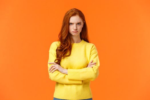 I am mad. Offended sulky cute and timid redhead curly girl, cross arms chest, sulking angry and tensed, frowning stare disappointed someone sad rude words, standing orange background insulted.