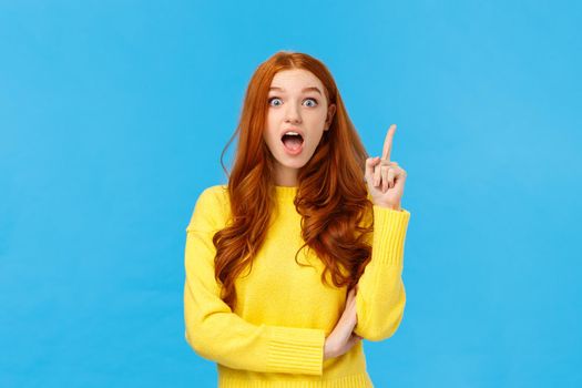 Got idea, listen. Excited creative redhead girl inspired, have plan or suggestion, raise index finger eureka gesture and speaking her solution, standing blue background enthusiastic.
