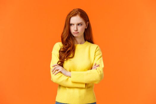 Offended angry and tensed woman with curly red hair, freckles, having bad mood, cross arms chest, thinking troublesome situation, frowning getting mad, standing orange background distressed.