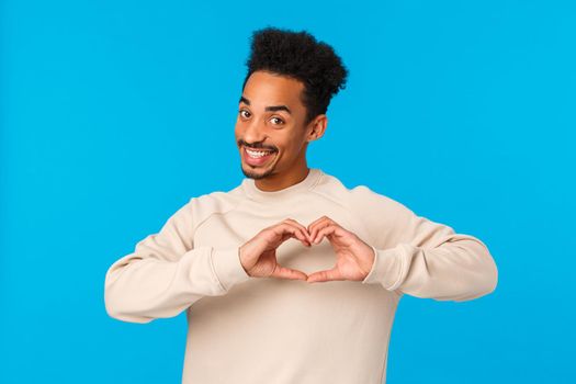 I love you. Cheerful and cute enthusiastic african-american smiling boyfriend making heart hands gesture near chest and grinning camera, make confession on valentines day, blue background.