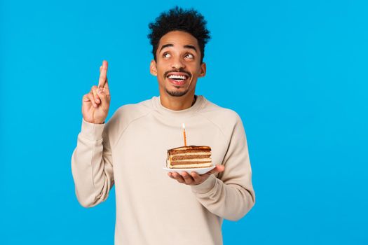 Man thinking what wish have idea. African american creative happy and excited guy raising finger eureka gesture smiling, holding b-day cake with candle, pondering, standing blue background.