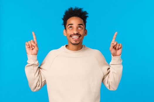 Wonderful promo. Amazed, excited smiling happy african american man with afro hipster haircut, moustache, looking pointing up admiring view, found excellent gift for valentines day, blue background.