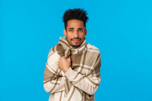 Its freaking cold outside. Upset african american guy feel unwell during winter holidays, looking left frowning unhappy and disappointed, cant come party caught flu, wrap himself blanket, blue wall.