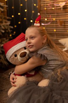 A girl hugs a bear toy in a Christmas cap bear Christmas kid child happy, for female young for play white fun, sleep plush. Gift woman happiness, relaxation wake