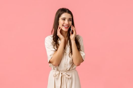Cheerful alluring and carefree happy woman in dress, laughing talking on phone, calling best friend and discuss romantic date, holding smartphone near ear, look sideways, pink background.