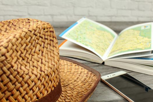 Straw hat, guide book with map, and mobile phone on gray wood desk. Travel planning concept.
