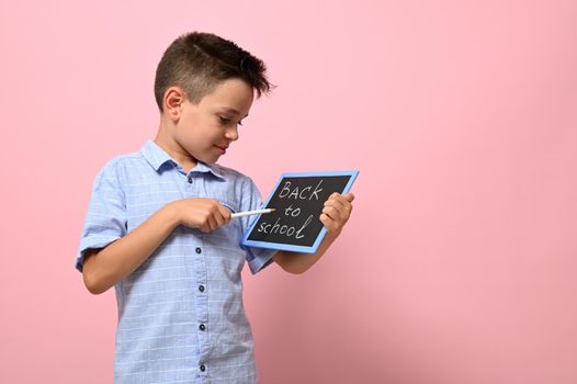 Lettering Back To School on a chalk board in the hands of a happy pupil. Isolated over pink background with copy space.Concepts