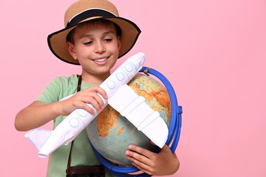 Adorable boy in summer hat holds an airplane and a globe in his hands and simulates the flight around the world. Tourism, travel and aviation concepts