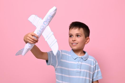 Handsome schoolboy playing with a paper airplane against pink background with space for text. Tourism, travel, geography knowledge concepts