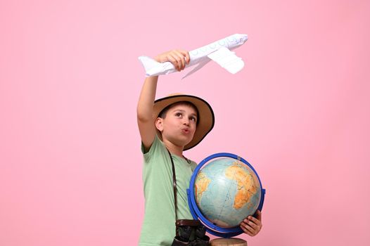 A cute schoolboy traveler holds a globe and an airplane in his hands, simulating a flight around the globe. Travel concept.