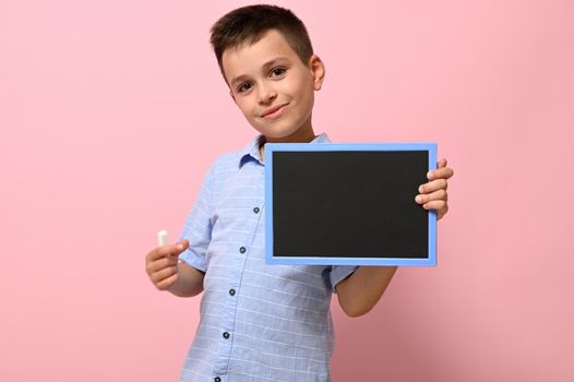 Isolated portrait on a pink background of a schoolboy with chalk and chalkboard in his hands. Back to school. Concepts