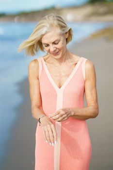 Beautiful mature woman walking along the shore of a tropical beach, wearing a nice orange dress. Elderly female enjoying her retirement at a seaside retreat.