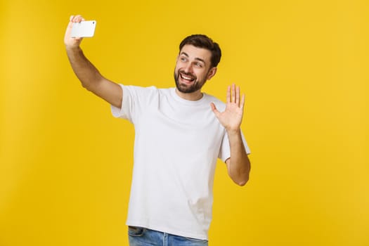 Closeup of young handsome man looking at smartphone and taking selfie. isolate over yellow background