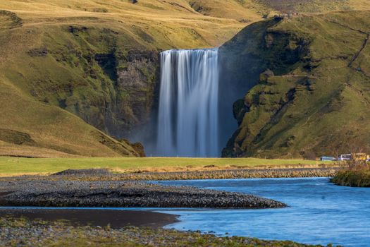 Long exposure of Skogafoss waterfall in Iceland from the distance with tourists hiking and blurred cars