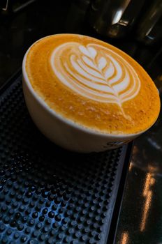 Tulip latte art on cafe latte on dark rubber mat