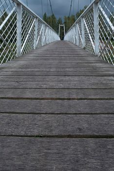Low view of the bridge. Wood paved and white fence bounded by a suspension bridge in the Donja Dubrava. The bridge is the last building at the Donja Dubrava hydroelectric power plant. The gloomy weather and low view seem to be the starting point of a long journey.