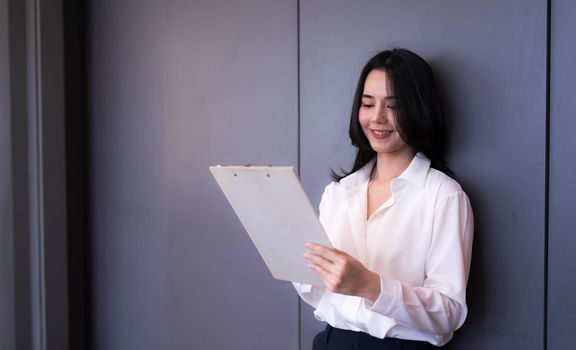 Asian young business female smailing and reading company earnings report in modern office.