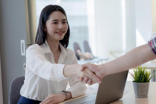 Asian young businesswoman shaking hands with a business partner after a successful collaboration in bright office. Teamwork Deal Cooperation Partnership business people concept.