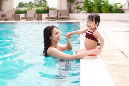 Mother and baby girl having fun in the pool. Summer holidays and vacation concept