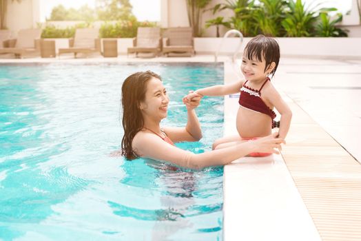 Mother and baby girl having fun in the pool. Summer holidays and vacation concept