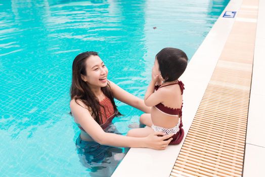 Mother and baby girl having fun in the pool. Summer holidays and vacation concept